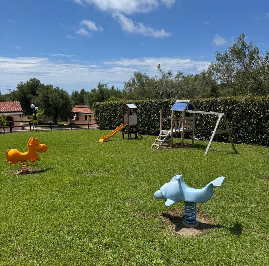 Parco giochi soleggiato con altalene e scivolo, cielo blu e nuvole soffici.